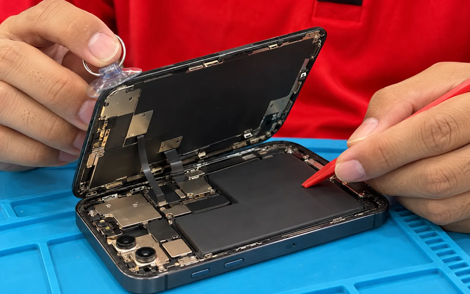 Technician opening a smartphone on the repair mat, display lifted with a suction cup