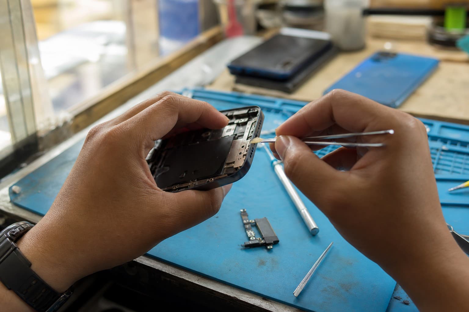Technician cleaning and inspecting an iPhone charging port with fine tweezers on a repair-shop bench